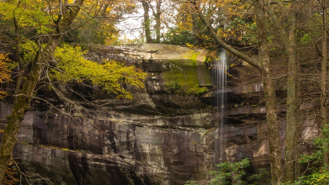 Rainbow Falls spilling over a tall rock ledge in autumn forest